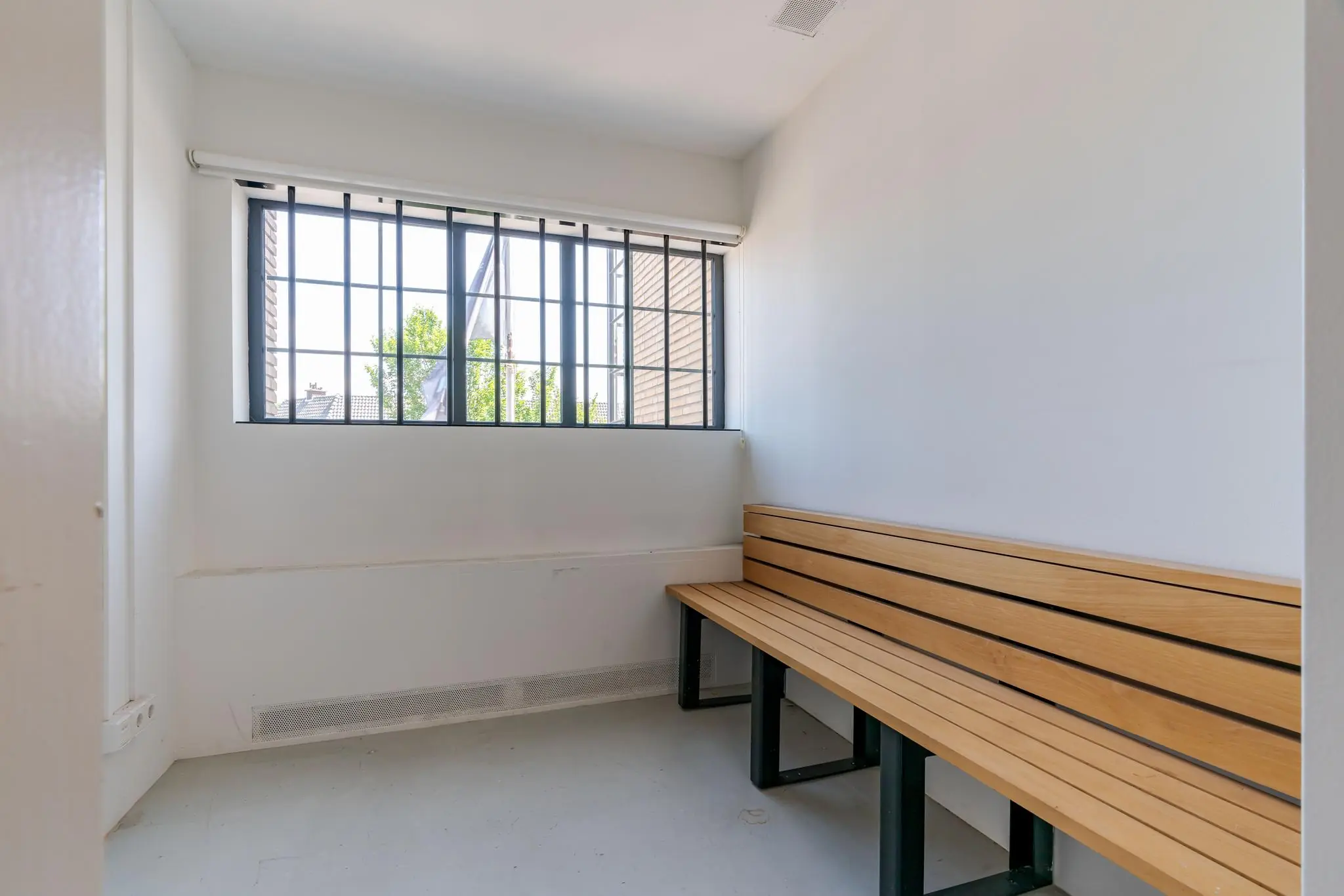 Kleine, witte wachtruimte met houten bank en tralies voor het raam aan de Van Alkemadelaan.